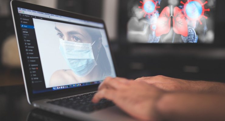Zdjęcie nawiązujące do epidemii koronawirusa – komputer z wizerunkiem kobiety w masce oraz w tle obraz przedstawiający płuca i wirusy