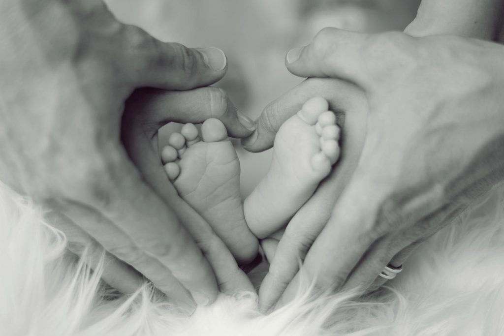 Grafika przedstawiająca ręce kobiety i mężczyzny obejmujące stópki niemowlaka.