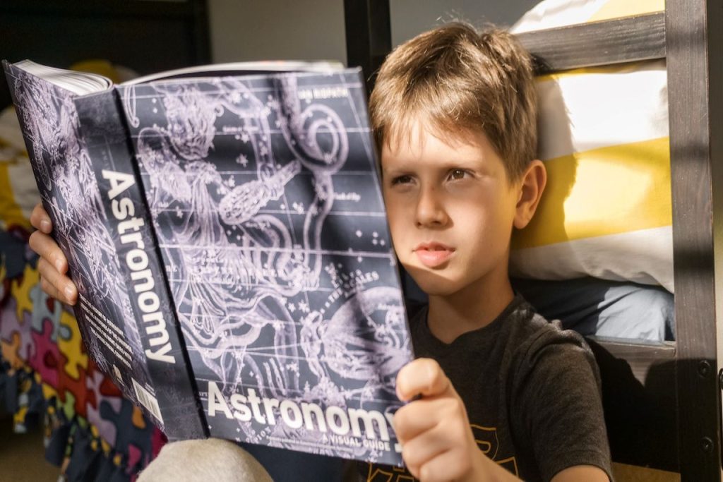 Grafika przedstawiająca chłopca czytającego książkę o astronomii.