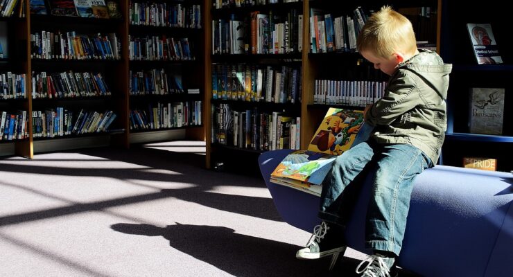 grafika przedstawiająca chłopca czytającego książkę w bibliotece